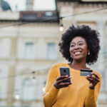 Happy woman walking holding a phone and credit card