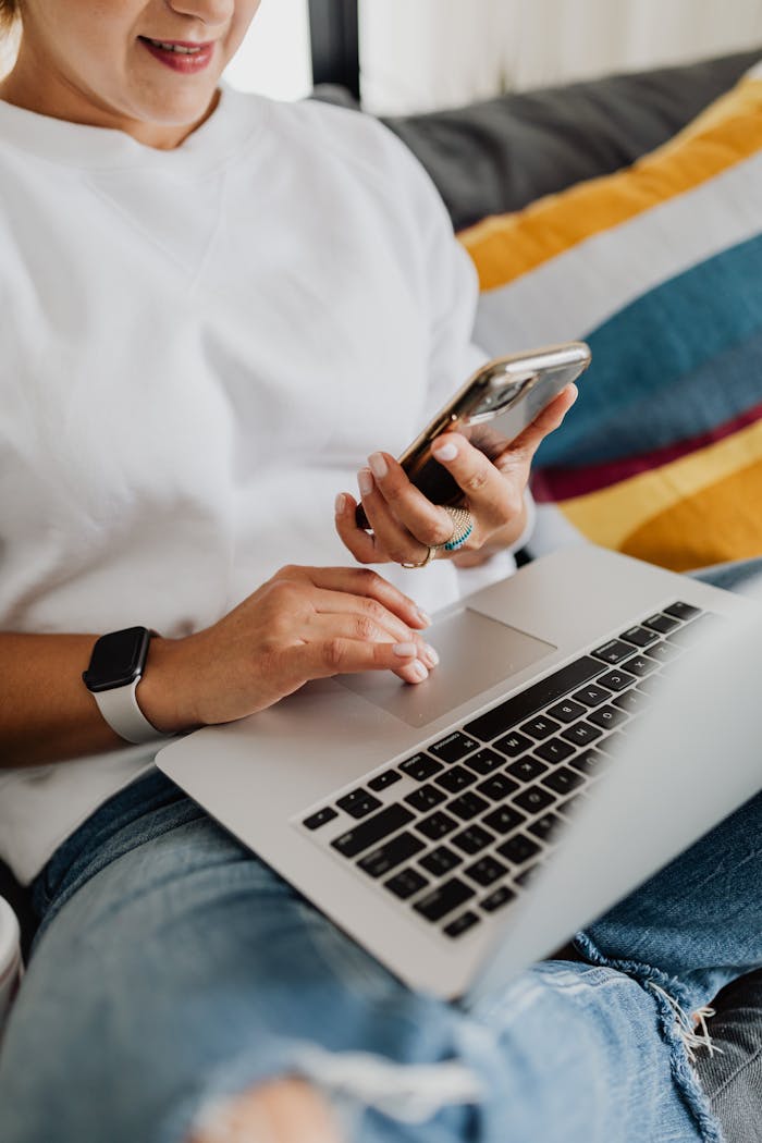 A person multitasking with a laptop and smartphone while sitting on a couch, embodying remote work lifestyle.