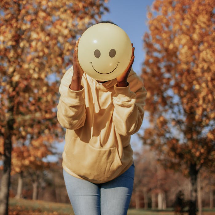 Person with smiley balloon in autumn park, exuding joy and playfulness.
