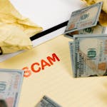 Yellow notebook with 'Scam' text surrounded by crumpled paper and banknotes.